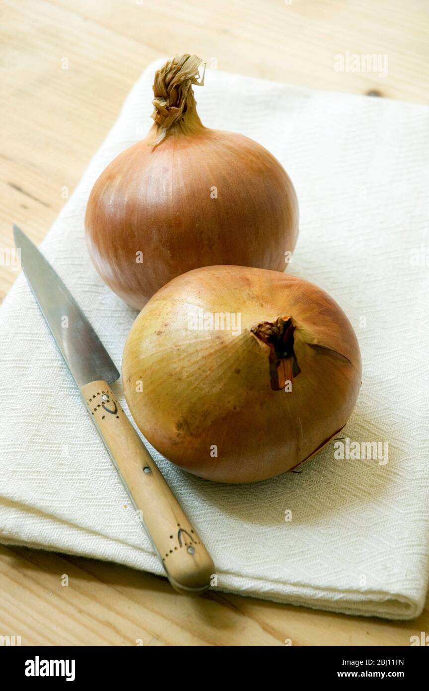 Zwei Zwiebeln auf cremigem weißen Leinentuch mit kleinem französischen Messer - Stockfoto