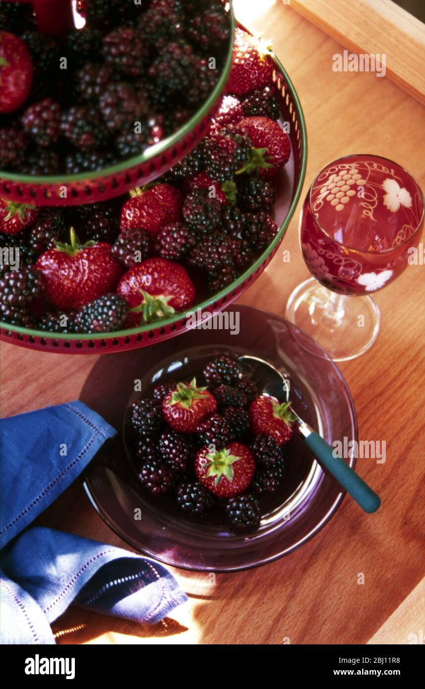 Erdbeeren und Brombeeren auf hohem Ständer mit Weinglas und Teller - Stockfoto