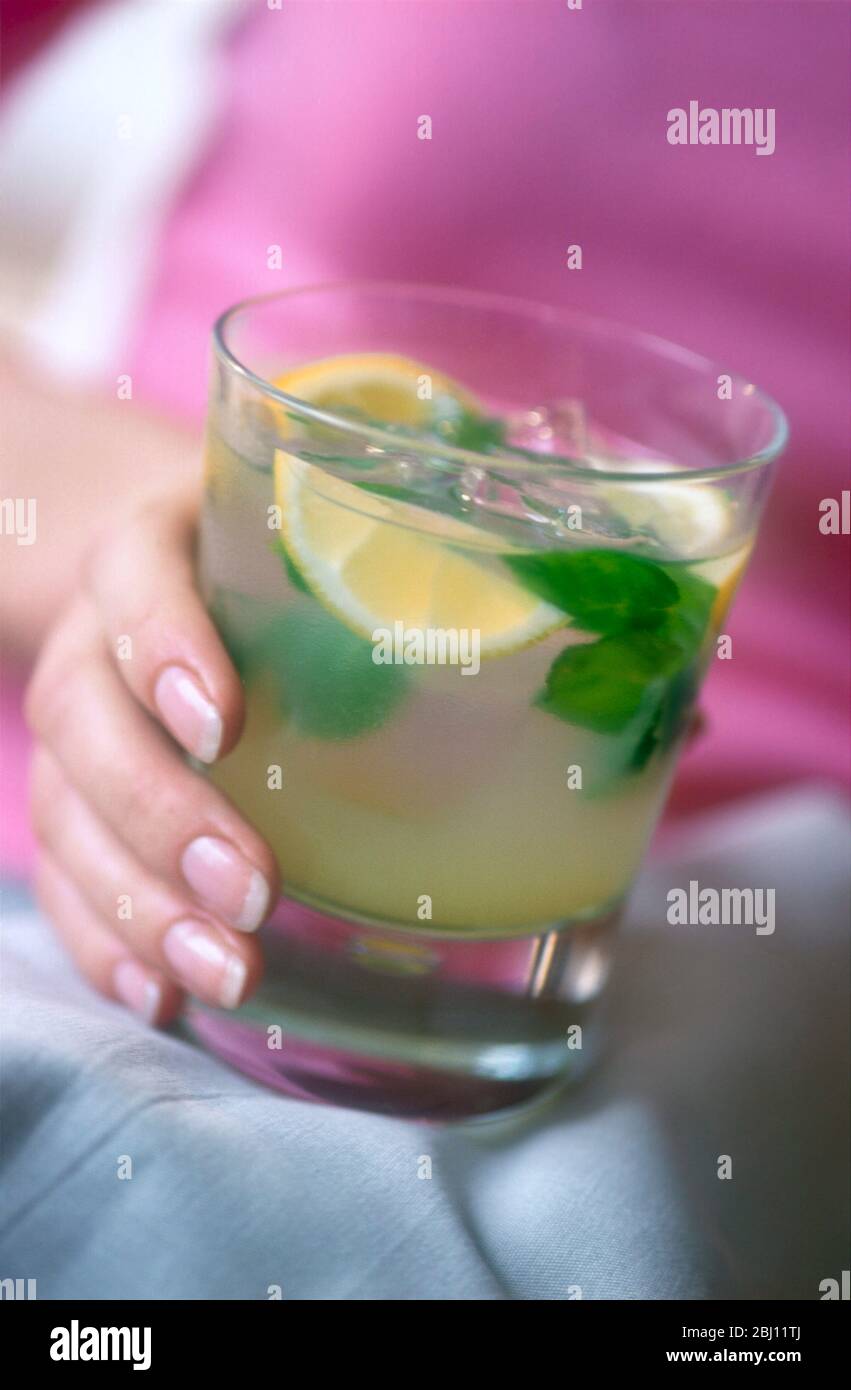 Ein Glas Gin-Cocktail in der Hand auf dem Schoß des Mädchens - Stockfoto
