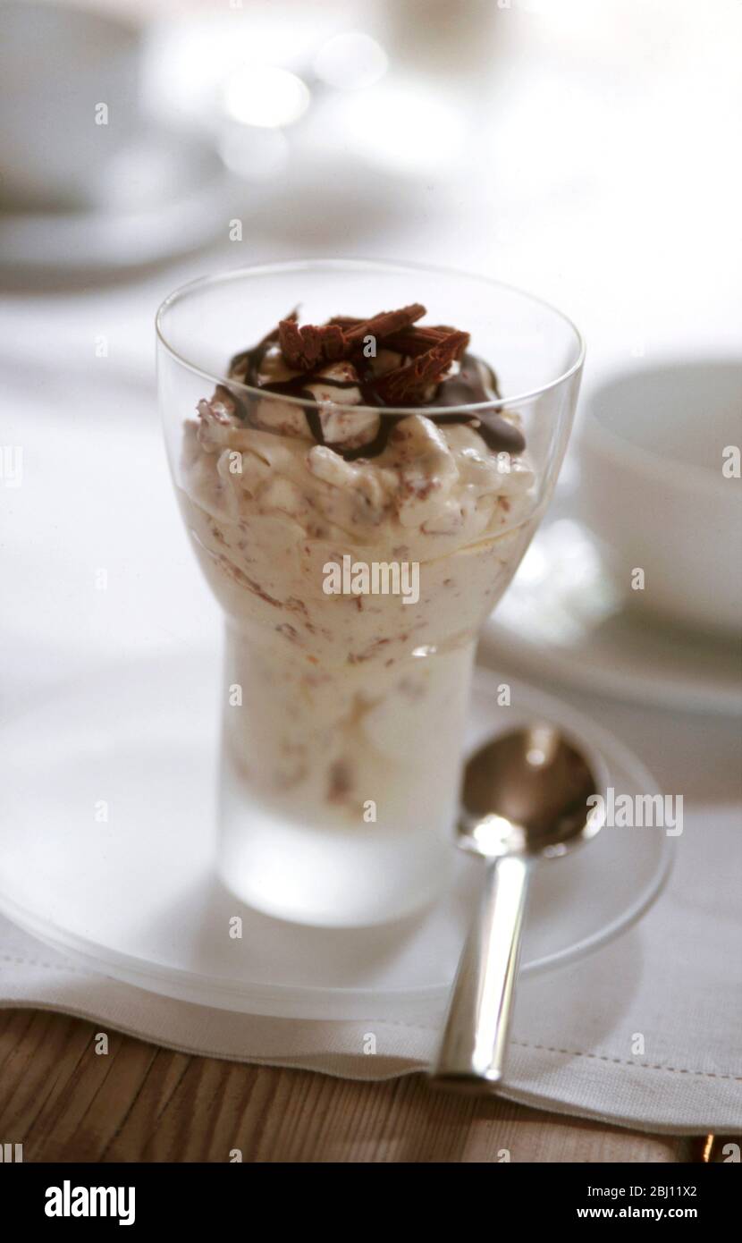 Schokolade und Sahnedessert in modernem Glas auf kleinem Glasteller in Tischgestellung - Stockfoto