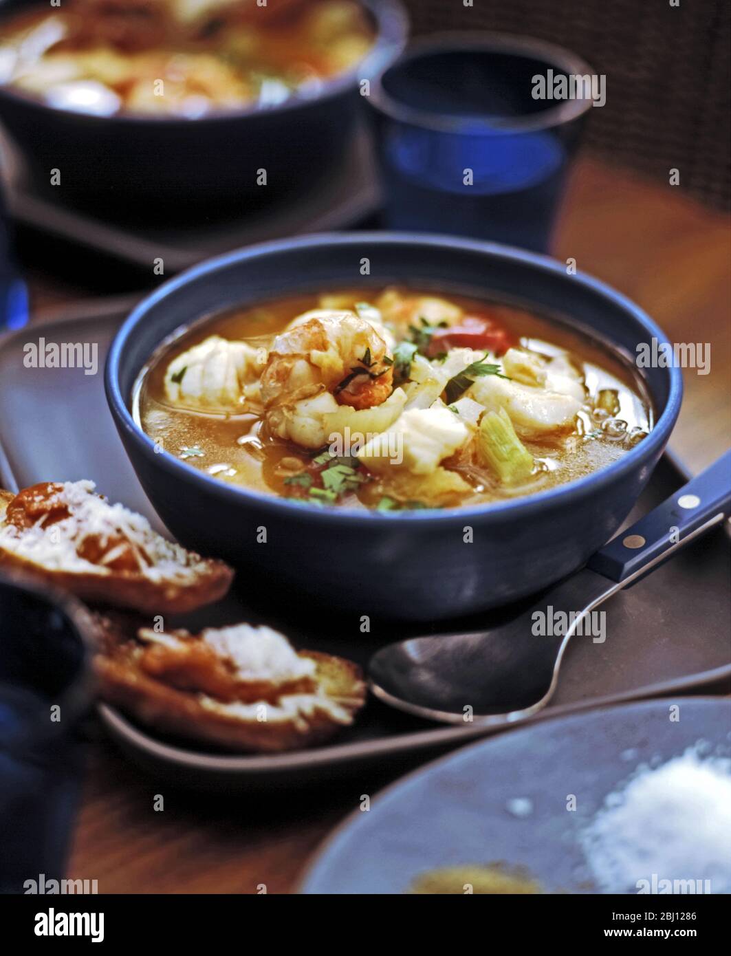 Fischsuppe aus Königskarnelen und Seeteufel mit Gemüse und Kräutern. Toast mit Rouille und Käse an der Seite - Stockfoto