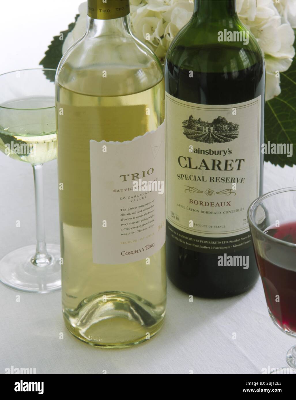 Flaschen und Gläser Rot- und Weißwein mit Hortensienblüte dahinter - - Stockfoto