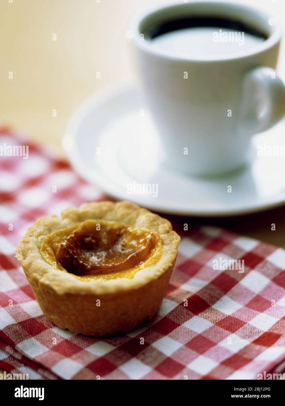 Traditionelle englische Pudding-Tart auf roter Gingham-Tischdecke mit einer Tasse schwarzen Kaffee - Stockfoto