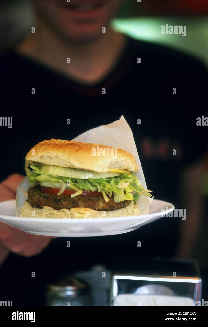 Klassischer Hamburger mit geschreddertem Salat und Zwiebelringen in Sesambrötchen auf weißem Teller, angeboten im Diner Restaurant - Stockfoto