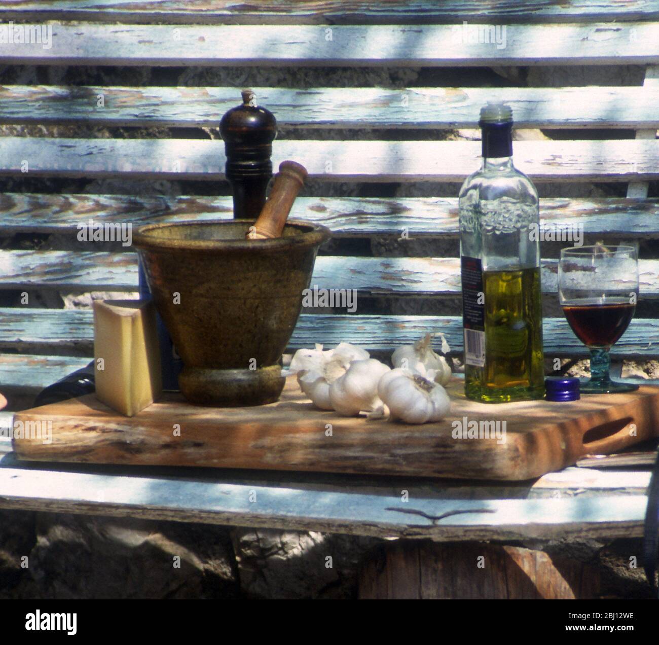 Zutaten im Freien - Olivenöl, Stößel und Mörser, Knoblauch - Rotwein, Pfeffermühle, Käse (Parmesan?) - - - Stockfoto
