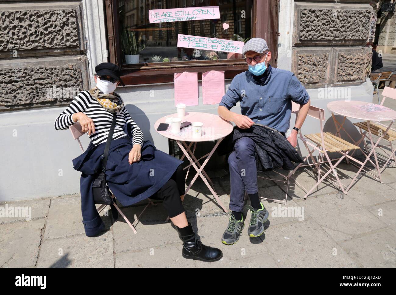 Krakau. Krakau. Polen. Coronavirus-Pandemie. Maskierte Leute mit Kaffee zum Abnehmen sitzen vor dem formell geschlossenen Café Verkauf nur Takeway. Stockfoto