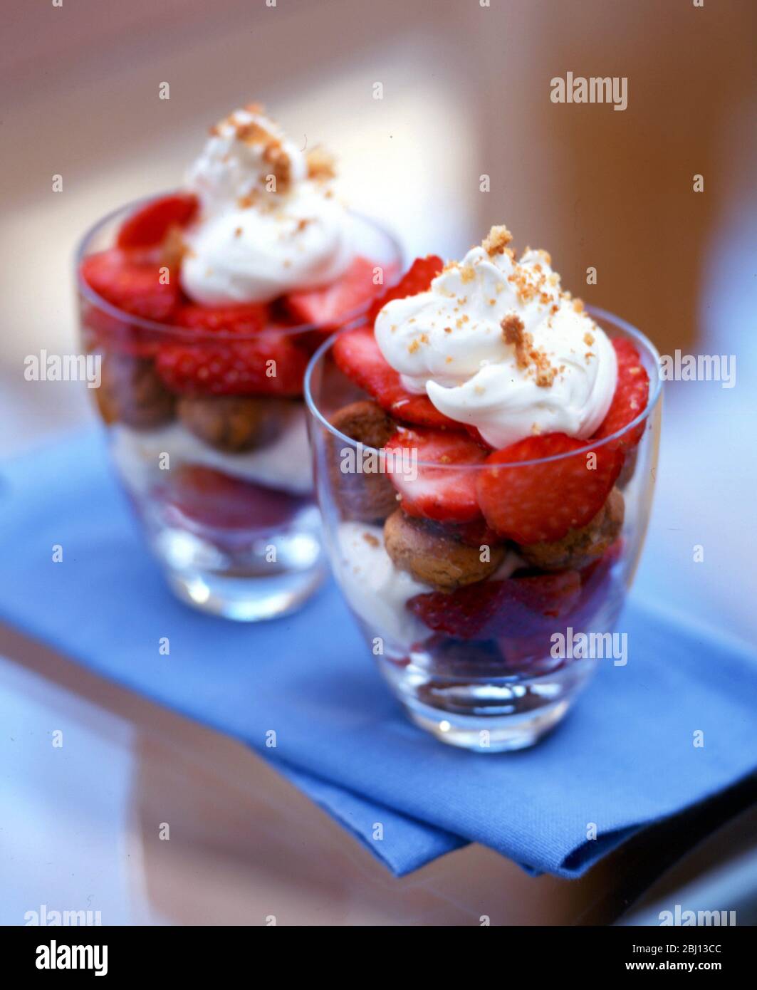 Sommerdessert von Ratafia-Keksen mit frischen, halbierten Erdbeeren und Schlagsahne mit gehackter Nussauflage - Stockfoto