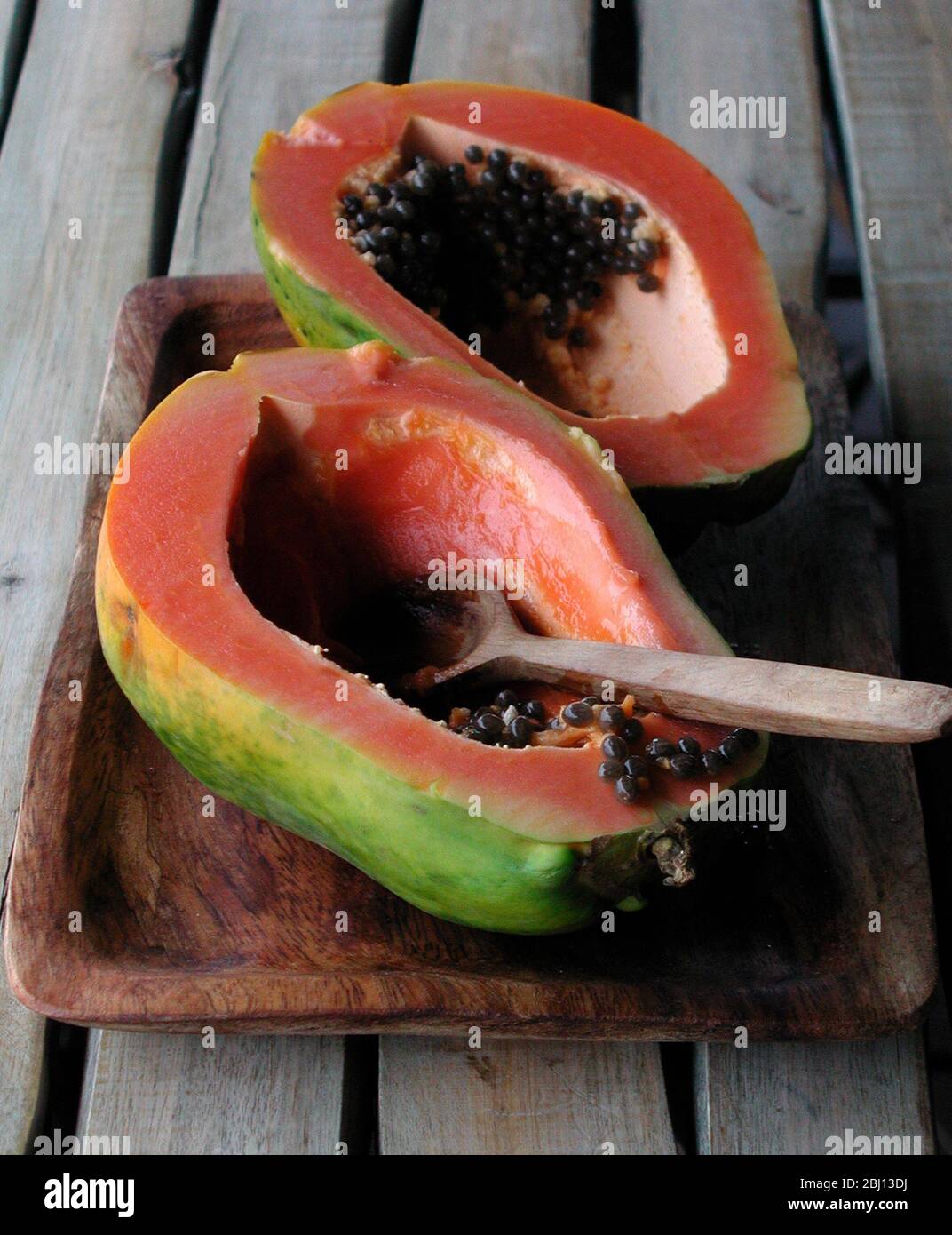 Halbierte Papaya-Früchte - Pips mit Holzlöffel ausräumen - Stockfoto