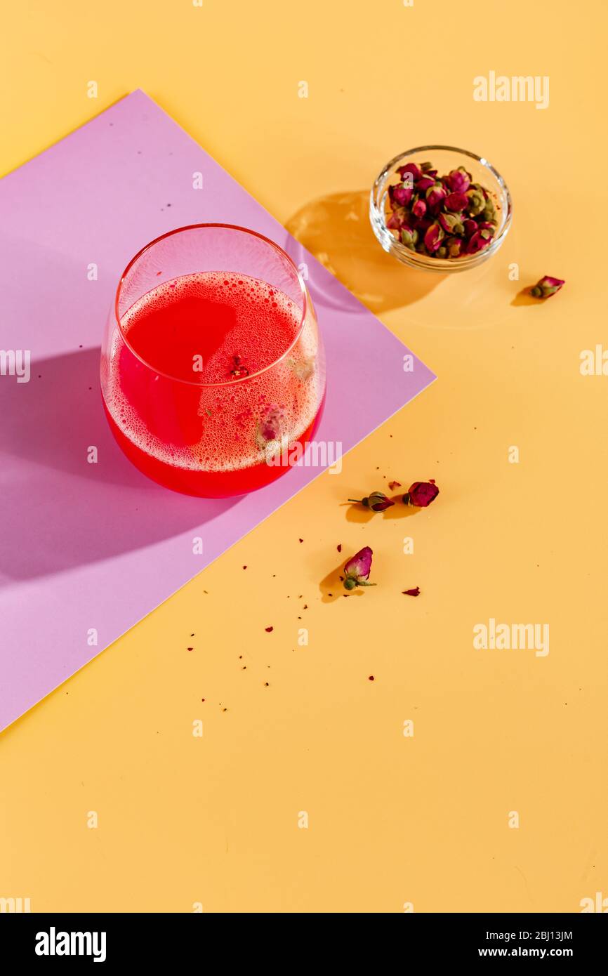 Rosa alkoholischen Cocktail mit Limonade, Champagner oder Martini mit trockenen Rosenknospen auf farbigem Hintergrund mit Blendung im Hintergrund dekoriert Stockfoto