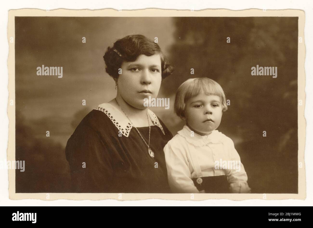 Anfang 1900 Foto von Jungen im Alter von etwa 3 Jahren mit bob Frisur, sitzt mit seiner Mutter, beide sehen ernst, Großbritannien um 1925 Stockfoto
