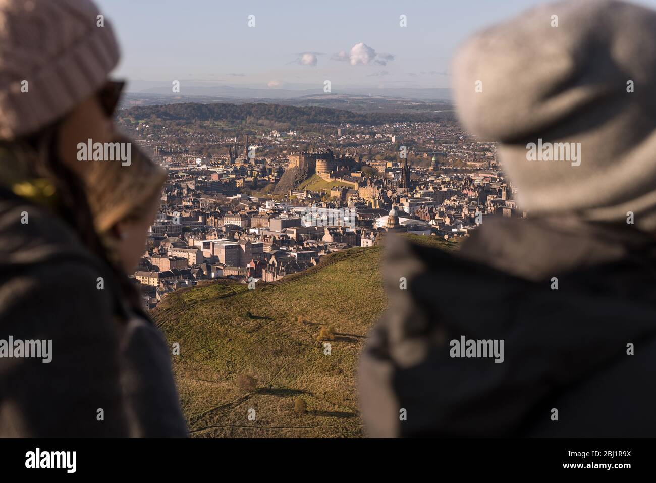 Eine Gruppe von Freunden auf dem Hügel Arthurs Seat mit Blick auf die Stadt Edinburgh und Edinburgh Castle, Schottland. Stockfoto