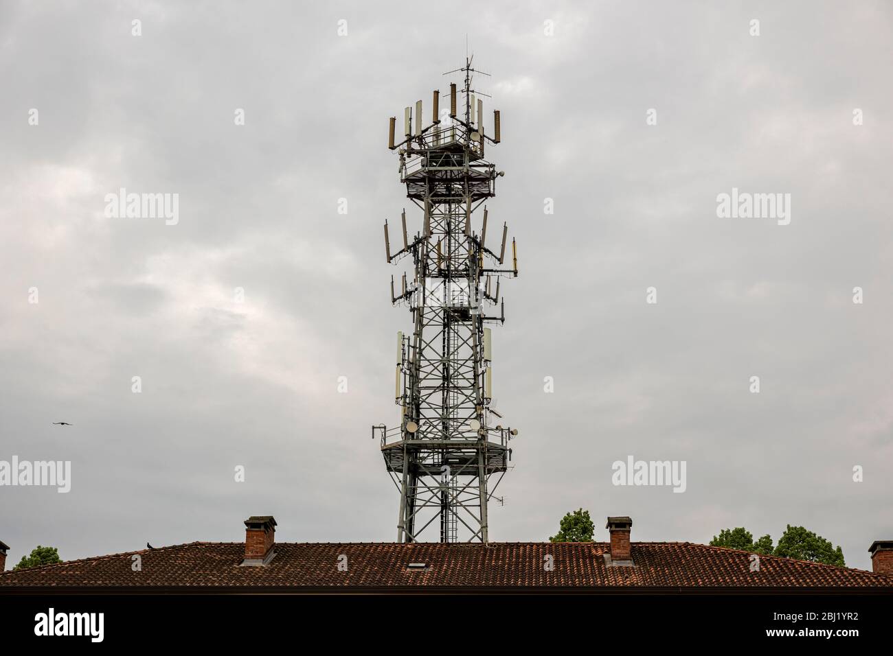 Antenne für Mobiltelefone hinter einem Hausdach. Mobilfunkturm an einem bewölkten Tag. Stockfoto