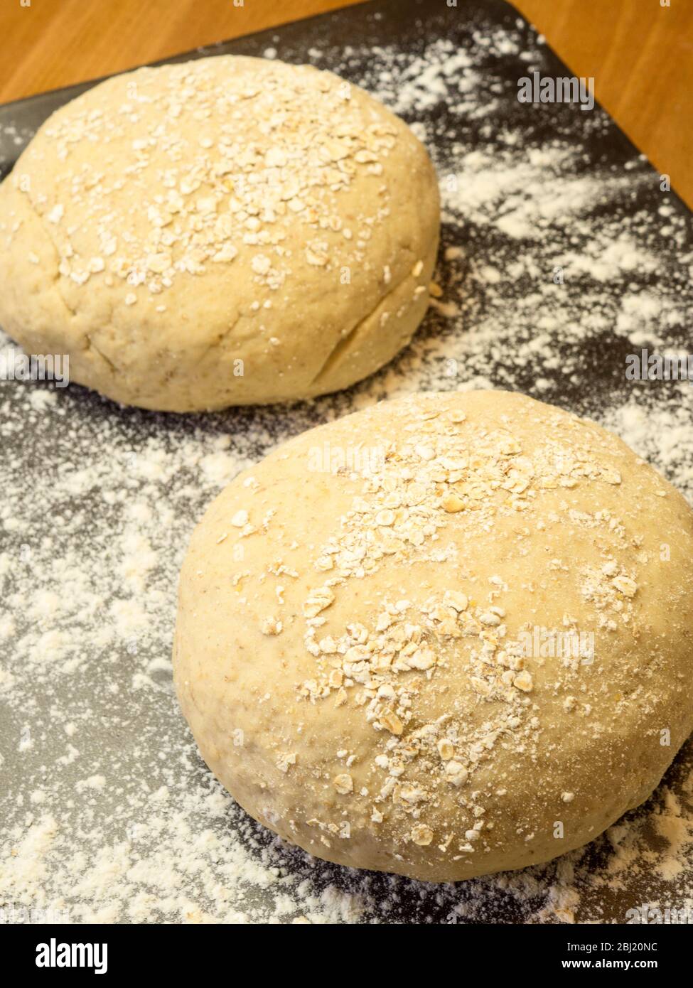 Zwei Runden Haferbrotteig in Hafer auf einem bemehlten Backblech auf einem Küchentisch gerollt Stockfoto