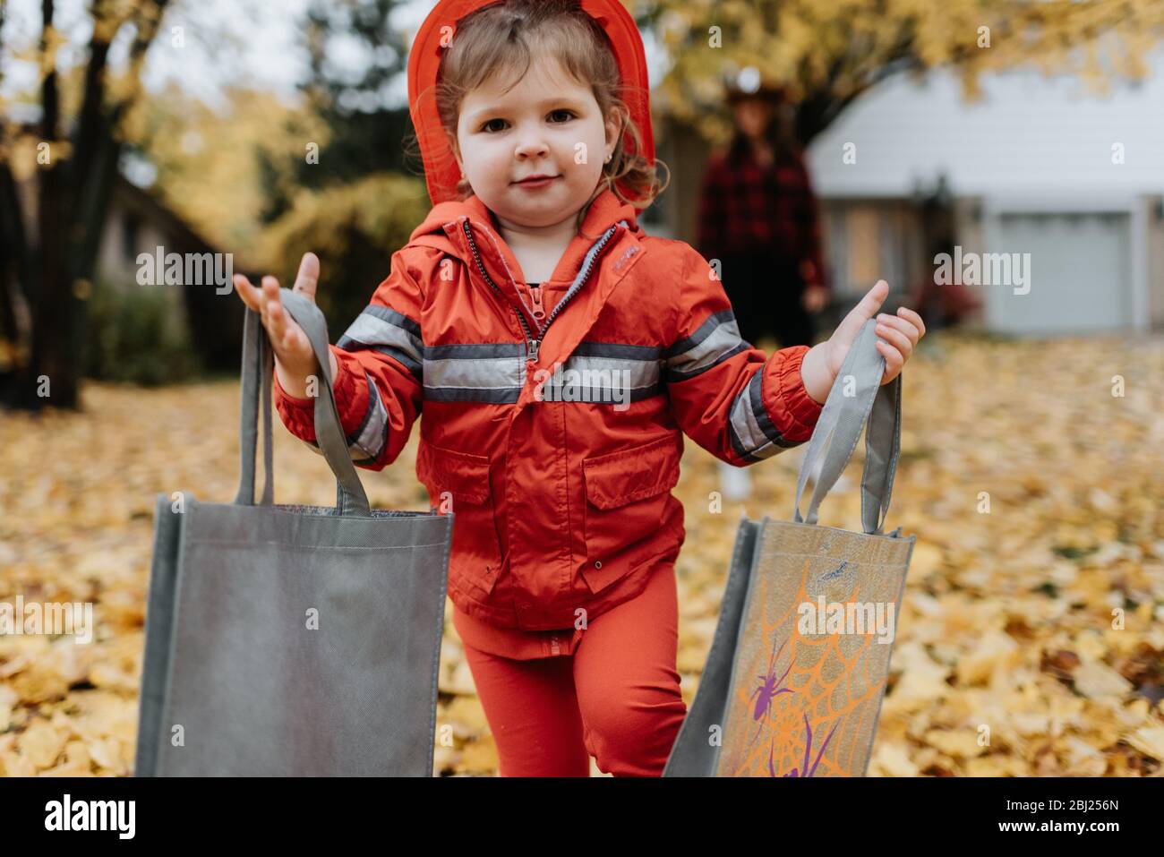 Ein Kind, das als Feuerwehrmann für Halloween gekleidet ist, geht durch einen Park mit Blättern auf dem Boden. Stockfoto