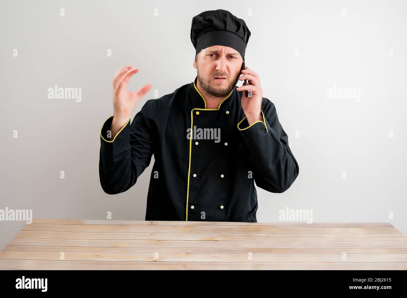 Porträt des jungen männlichen Koch in schwarzer Uniform mit braunen Haaren,  missfiel Gesicht und Gesten und sprechen auf Handy, posiert auf einem  weißen isoliert backgr Stockfotografie - Alamy