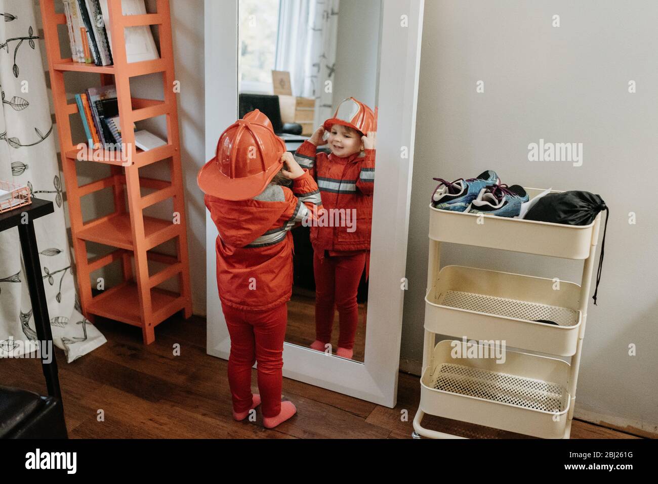 Ein Kind, das als Feuerwehrmann gekleidet ist und sich im Spiegel ansieht. Stockfoto
