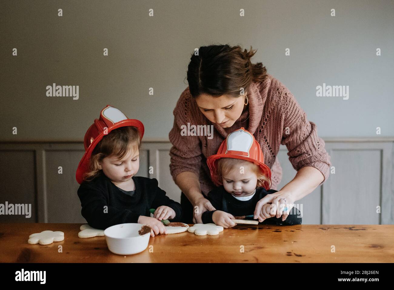 Eine Mutter hilft ihren beiden Kindern, Kekse mit Schokolade zu dekorieren. Stockfoto