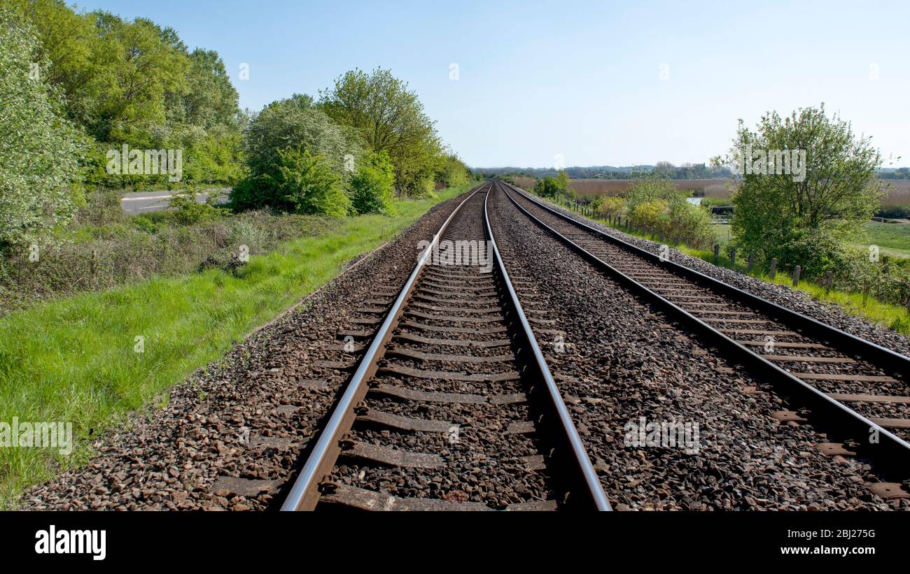 16.9 Ernte von parallelen Eisenbahnschienen in die Ferne mit üppigen grünen Bäumen umgeben, Büschen Straße unter blauem Himmel Stockfoto