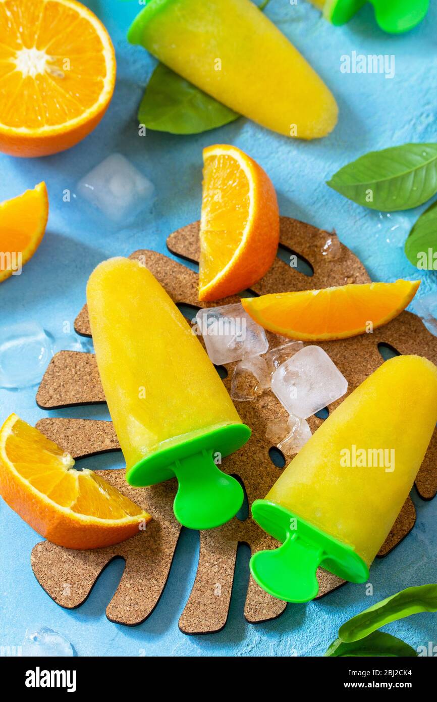 Hausgemachte Mops mit Orangensaft, Fruchteis, Lutscher auf blauem Stein- oder Schiefergrund. Stockfoto