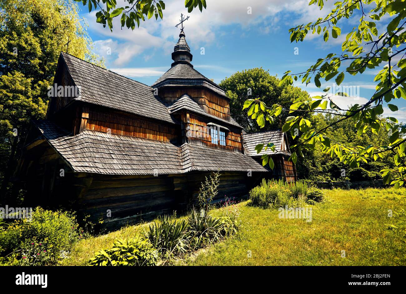 Alte Holzkirche, umgeben von üppiger Vegetation im traditionellen Dorf Osteuropa. Nationales Architekturmuseum in Pirogovo, Kiew, Ukraine Stockfoto