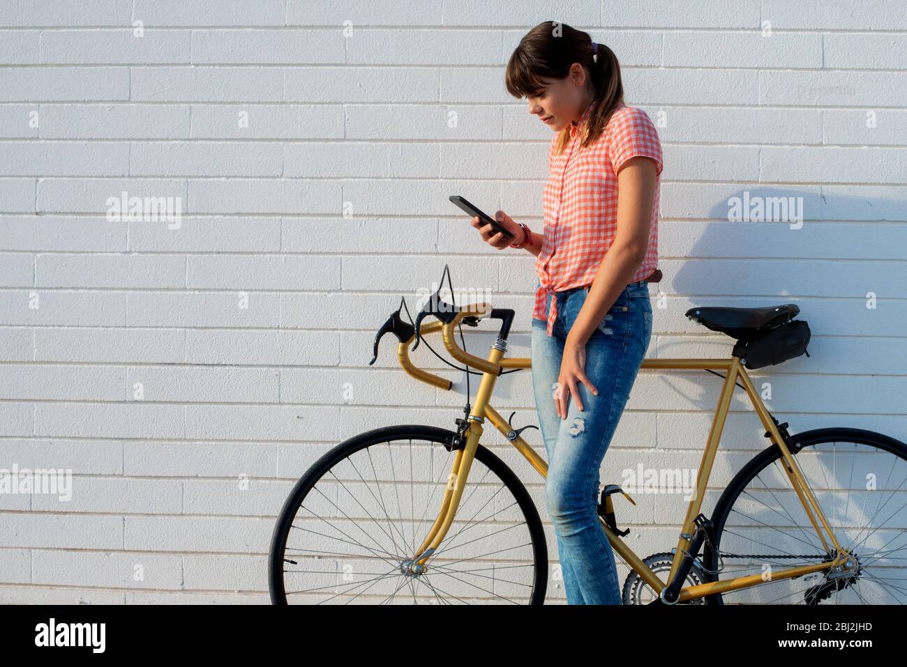 Mädchen mit Fahrrad berät ihr Smartphone an der weißen Wand Stockfoto