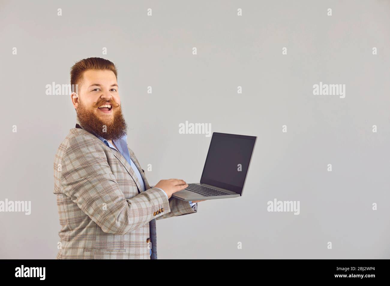 Lustige dicke Mann in einer Jacke arbeitet mit einem Laptop, während auf einem grauen Hintergrund stehen. Stockfoto
