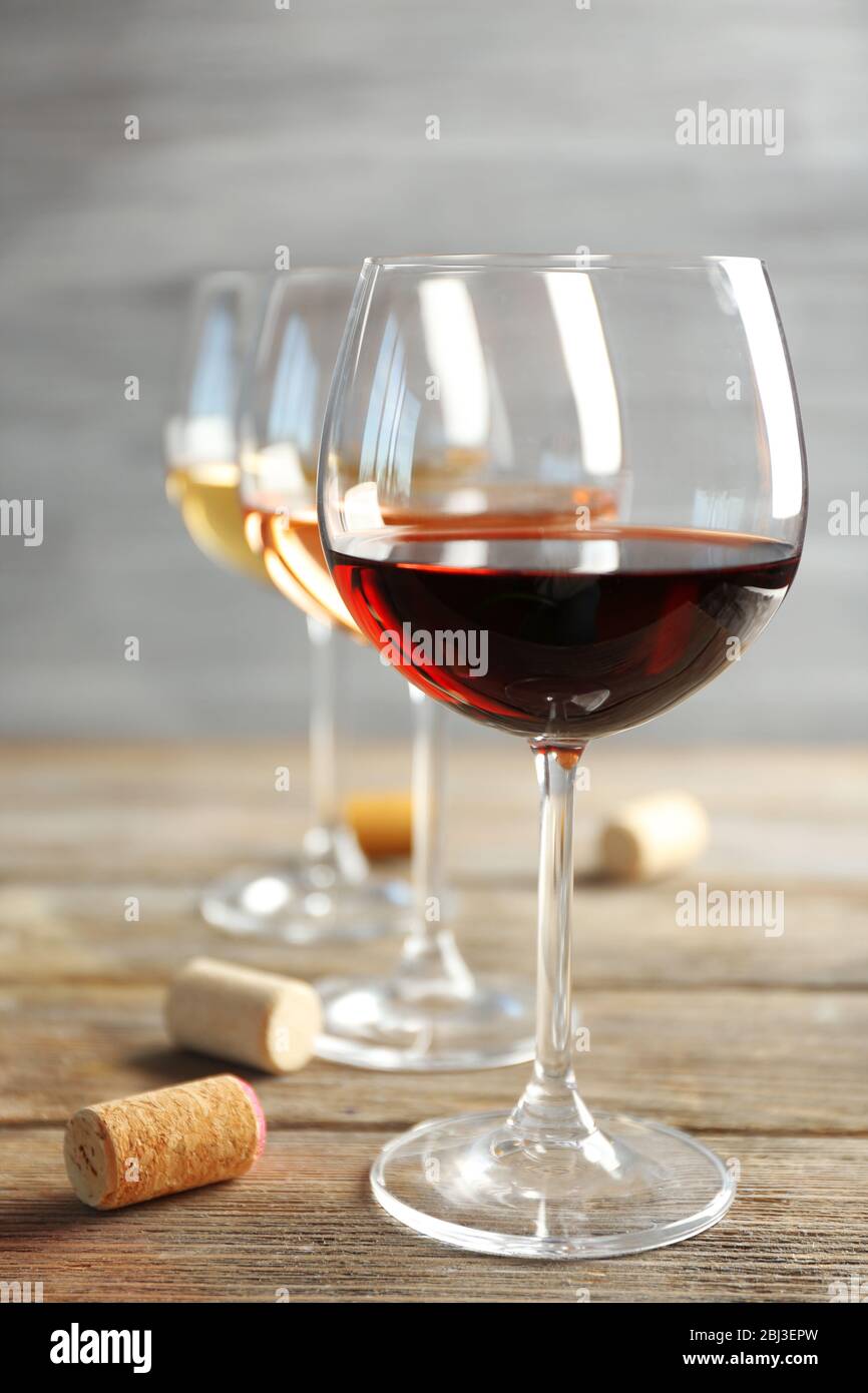 Weingläser in Reihe und Korken auf Holztisch vor grauem Hintergrund Stockfoto