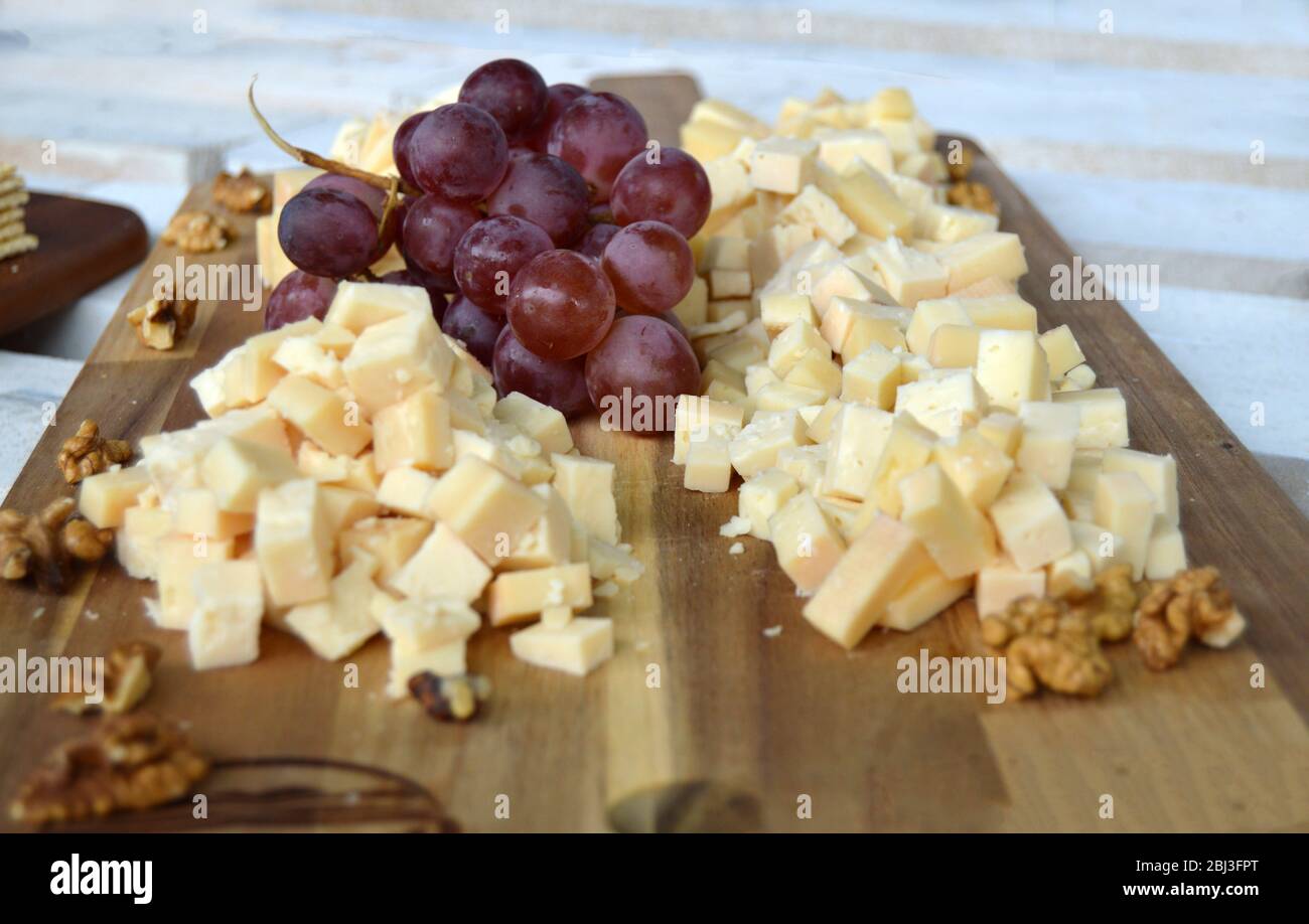 Eine Platte voller köstlicher Speisen für eine Käseverkostung, mit kleinen Stückchen Hartkäse, einer roten Traube und einigen Wandnüssen, natürlich und biologisch Stockfoto