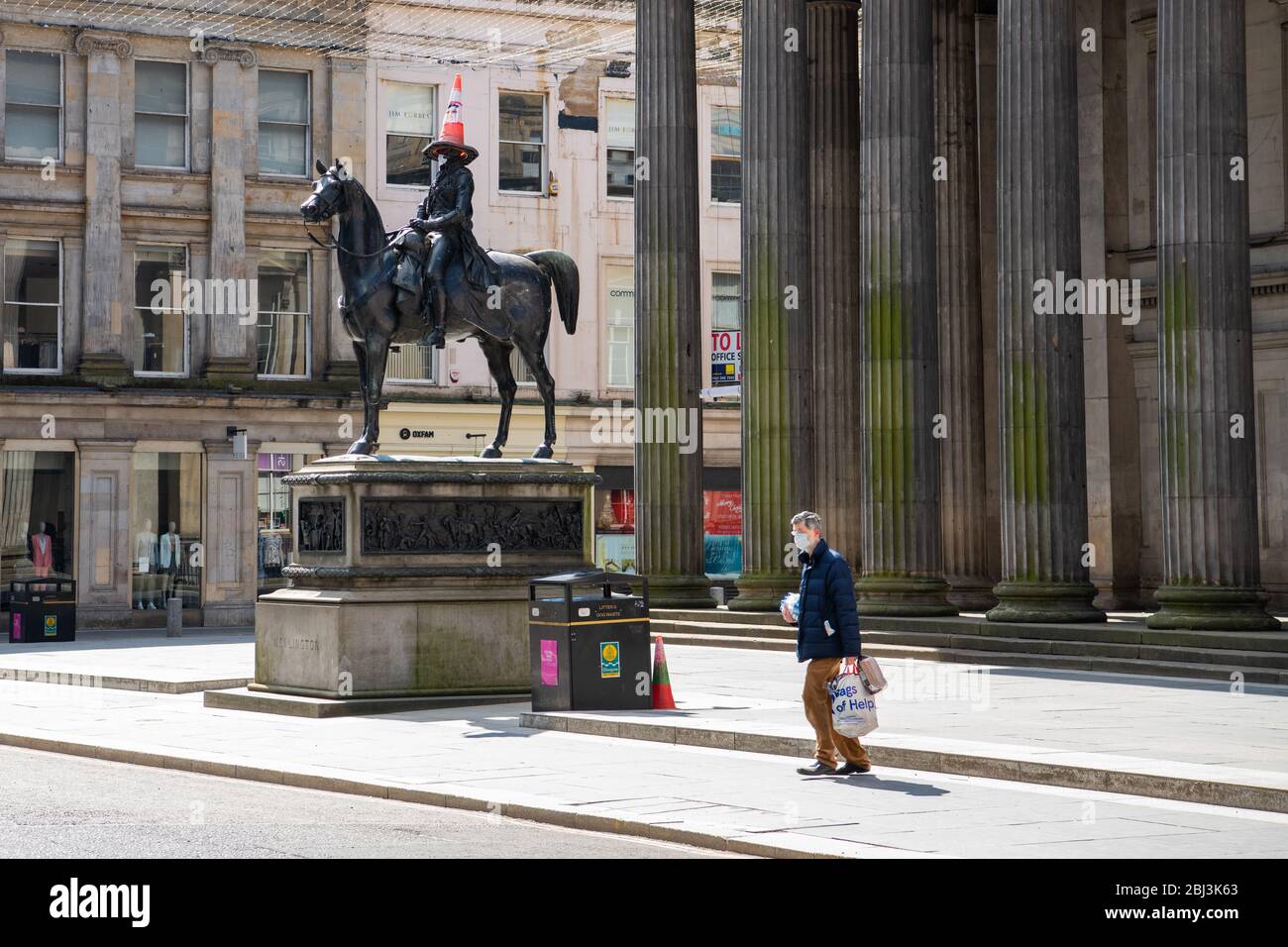 Glasgow, Schottland, Großbritannien. April 2020. Coronavirus Scotland UK: Ein Shopper mit Gesichtsmaske fährt an der ikonischen Duke of Wellington Statue in Glasgow vorbei und trägt auch eine Maske wie die schottische Regierung sagt, dass Schotten beim Besuch von Geschäften oder mit öffentlichen Verkehrsmitteln in Betracht ziehen sollten, Gesichtsbedeckungen zu tragen. Quelle: Kay Roxby/Alamy Live News Stockfoto