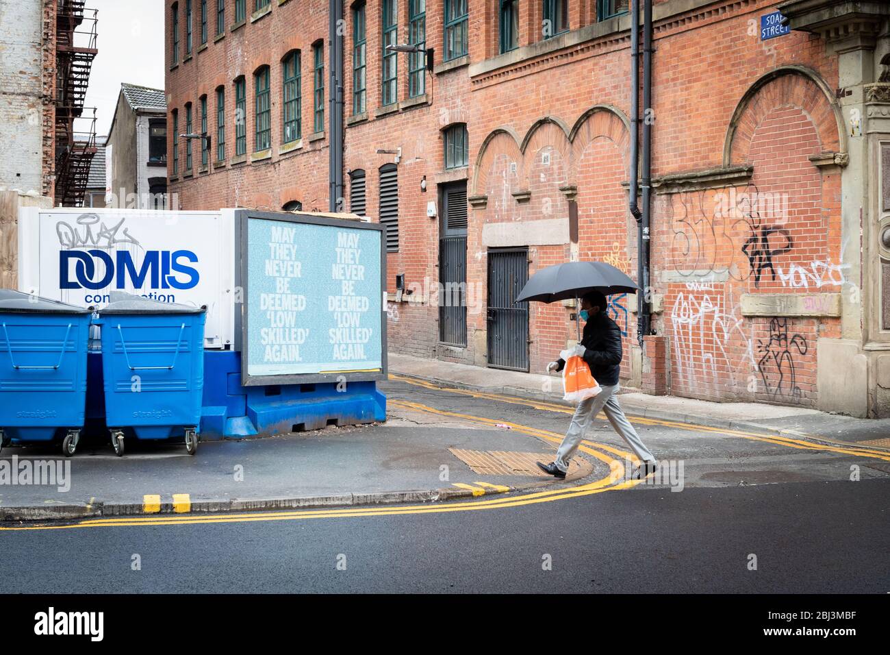 Manchester, Großbritannien. April 2020. Eine Person mit einer Maske geht an einem Plakat vorbei, das aufgrund von COVID-19 aufgestellt wurde. Seit Beginn der Blockierung des COVID-19 wurde Straßenkunst in der ganzen Stadt eingeführt. Kredit: Andy Barton/Alamy Live News Stockfoto