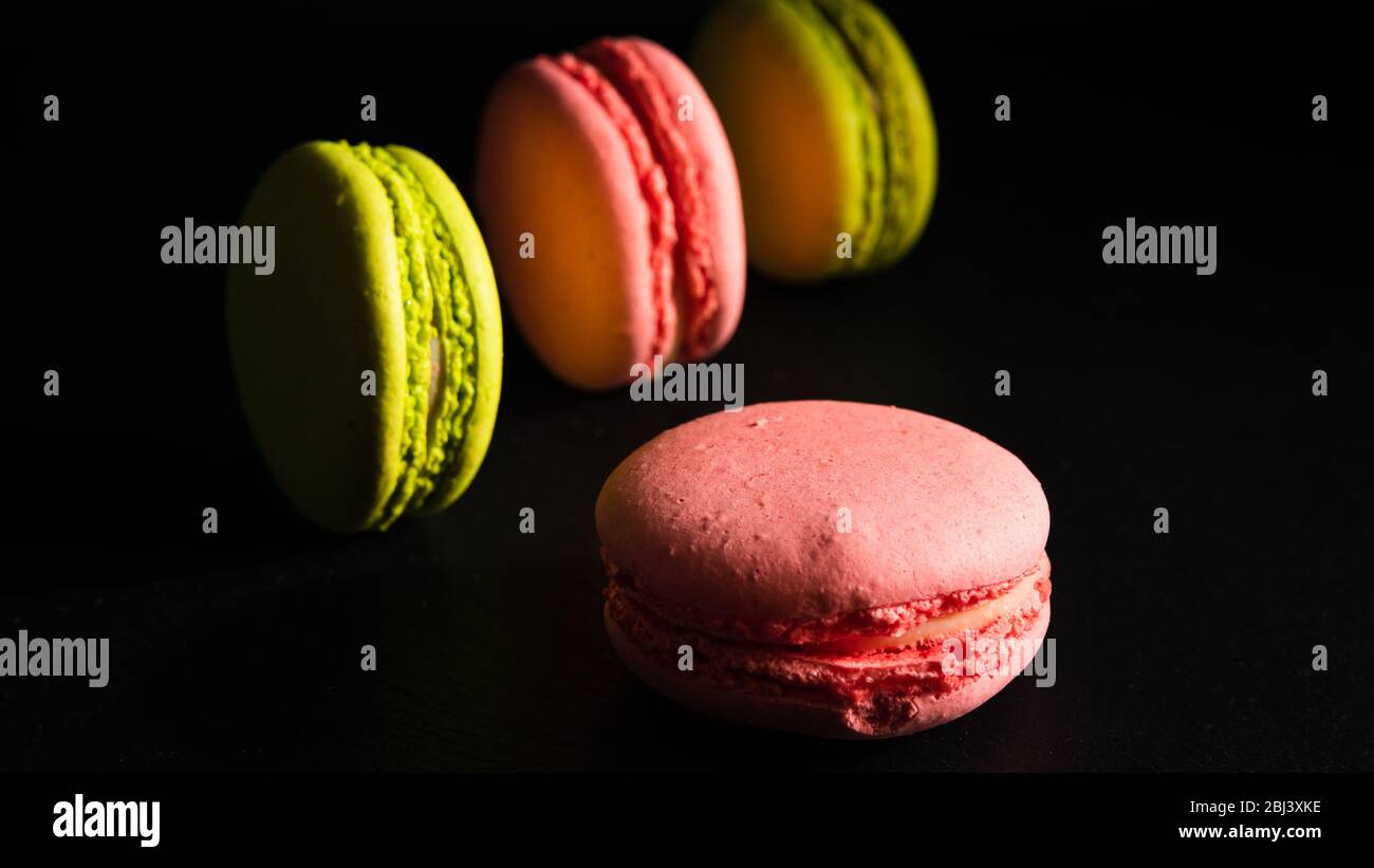 Süßes Werbekonzept, französisches Dessert - rosa und Pistazien Makronen auf schwarzem Hintergrund, Nahaufnahme Stockfoto