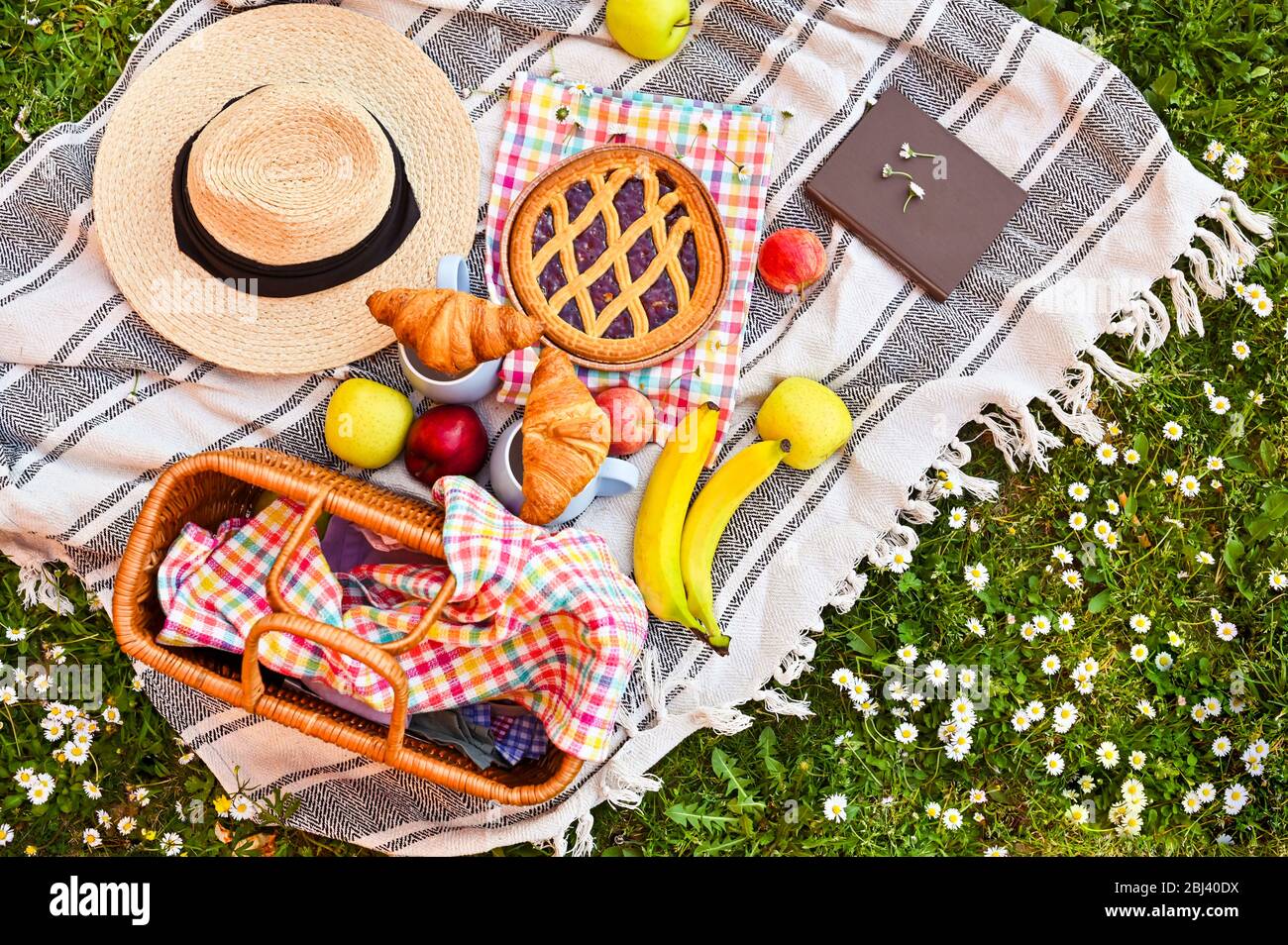 Picknickkorb auf dem grünen Gras im Park. Leckeres Essen zum Mittagessen im Freien. Süßes Gebäck, Getränke und Obst. Schöner Tag im Sommer. Oben. Kopierbereich. Weichstellung. Stockfoto