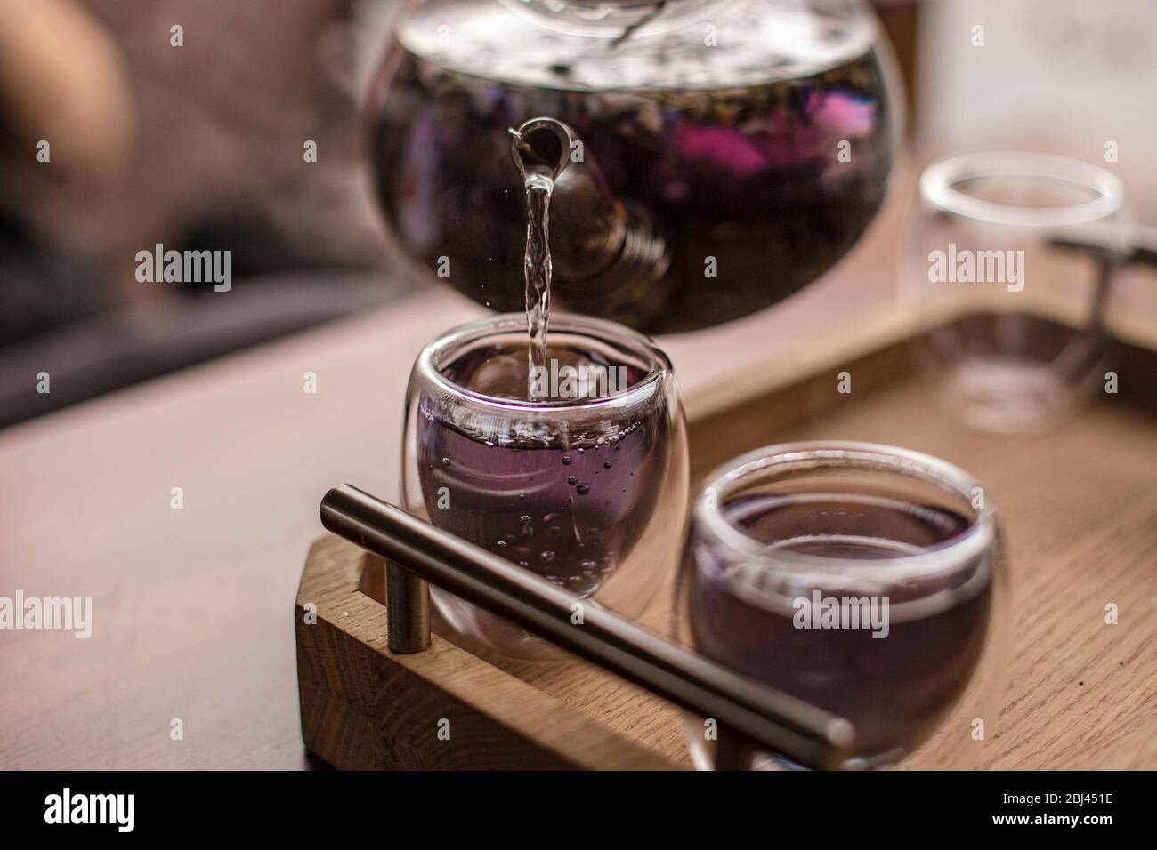 Der violette florale Kräutertee wird vom Brauer in die Tasse gegossen. Stockfoto