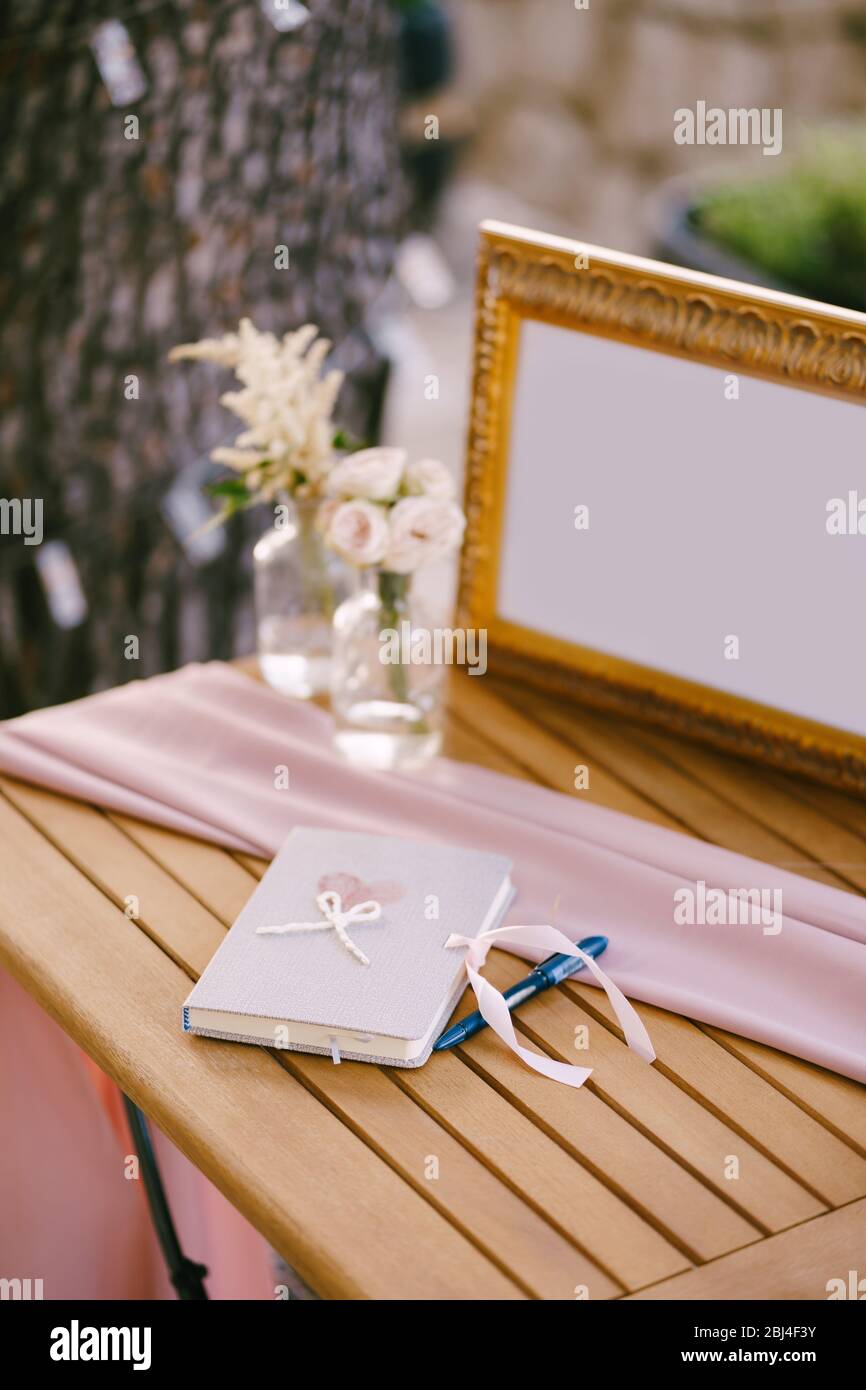 Album für Hochzeitswünsche. Ein Notizbuch für Hochzeitswünsche, ein blauer Stift, Blumen in einer Vase aus Wasser und ein Rahmen mit einem Foto. Stockfoto