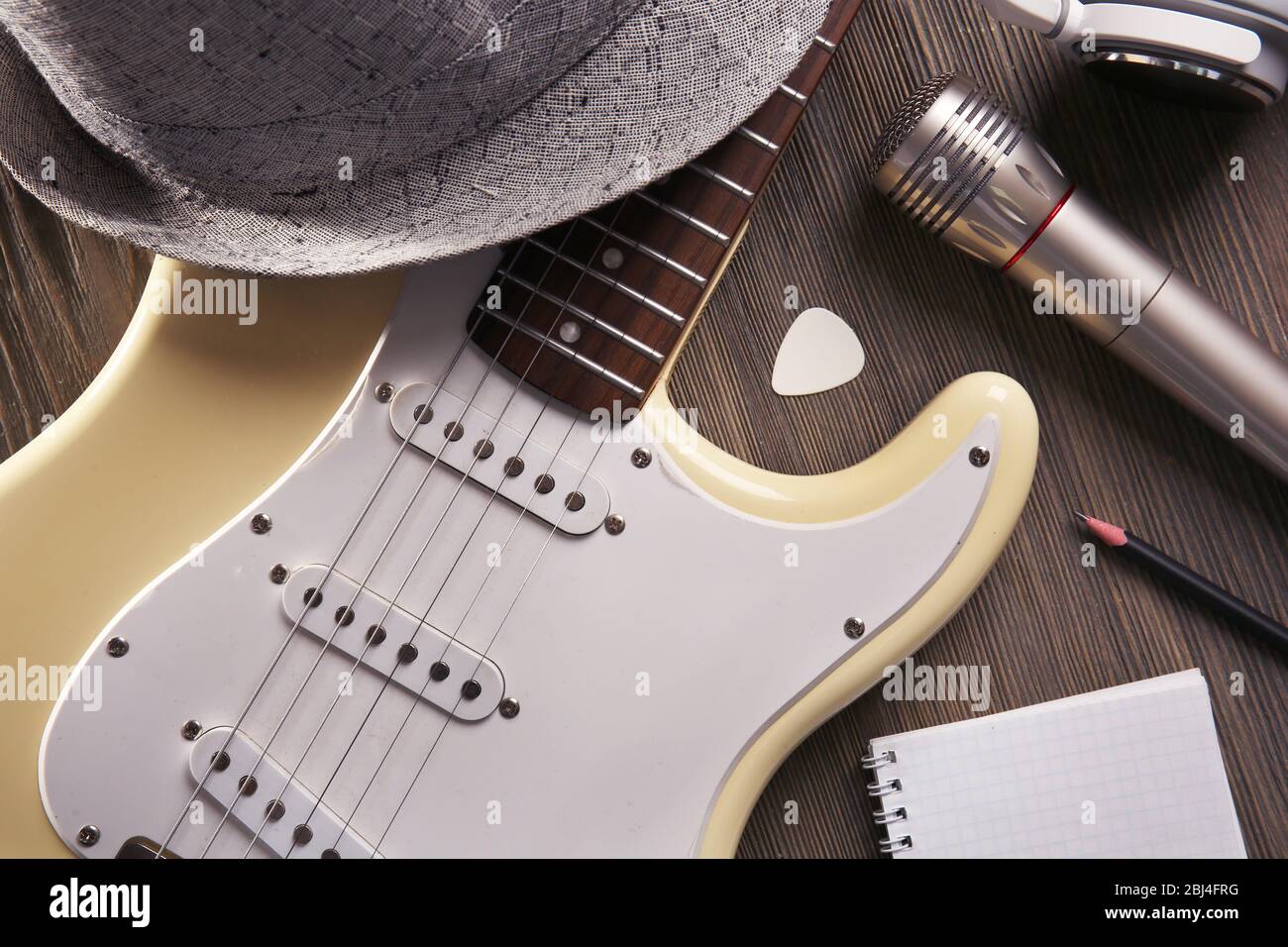 E-Gitarre mit Kopfhörer, Hut und Mikrofon auf Holzhintergrund, Nahaufnahme Stockfoto
