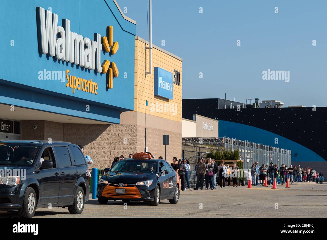 Vorderseite eines Walmart Superstore mit Menschen aufgereiht draußen aufgrund der globalen Pandemie von COVID-19 und soziale Distanzierungsrichtlinien. Stockfoto