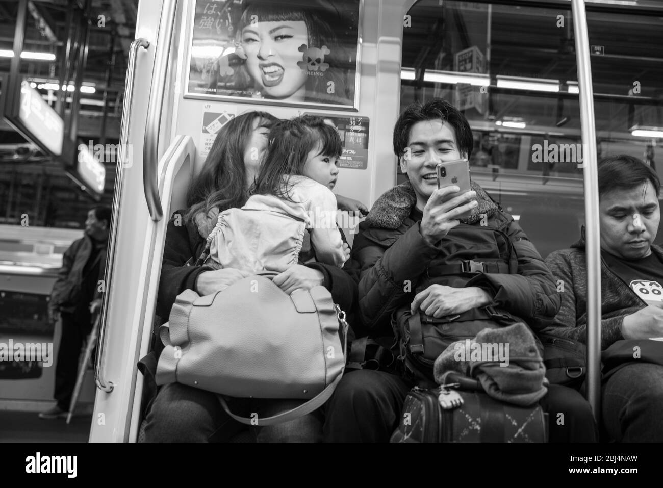 Eltern mit ihrem kleinen Kleinkind fahren mit dem Zug nach Hause und unterhalten das Kind mit ihrem Smartphone in Tokio, Japan. Stockfoto