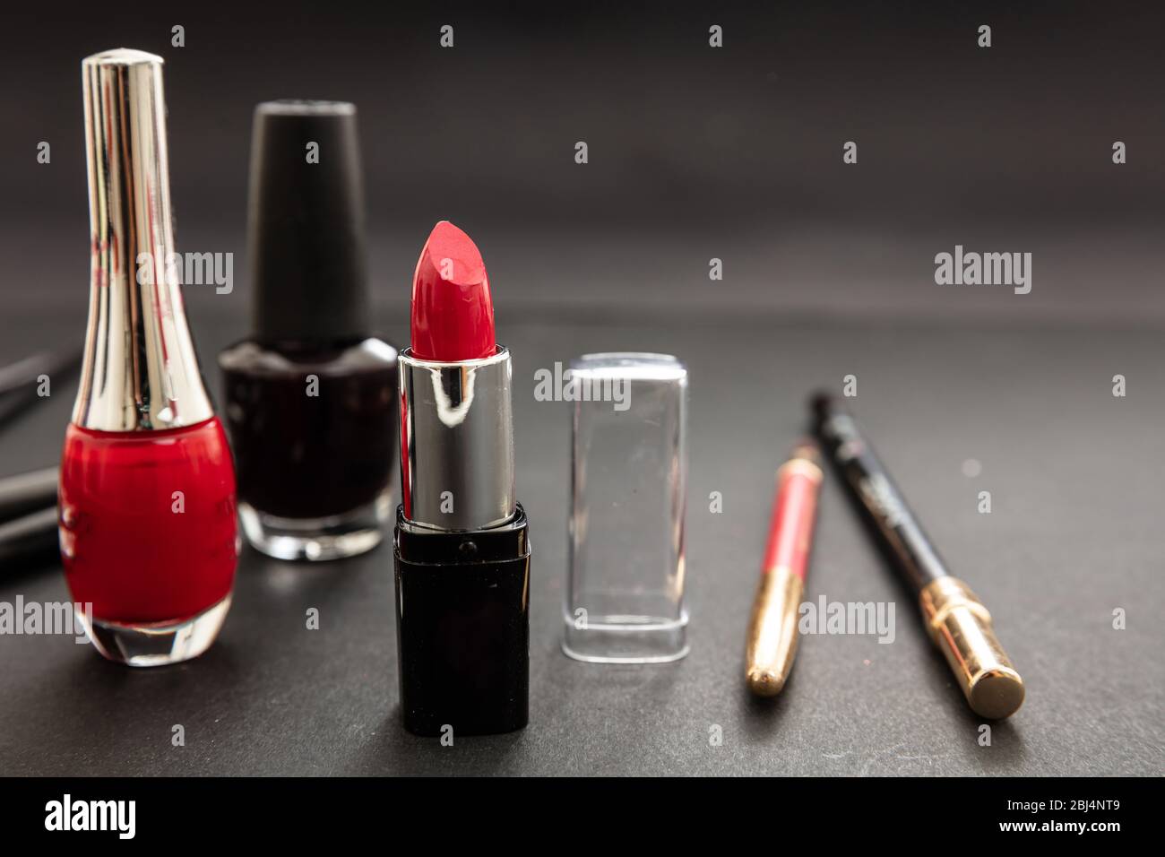 Kosmetikprodukte in Rot und Schwarz herstellen. Roter Lippenstift und nagellack, Augenstift und Bürsten vor schwarzem Farbhintergrund Stockfoto