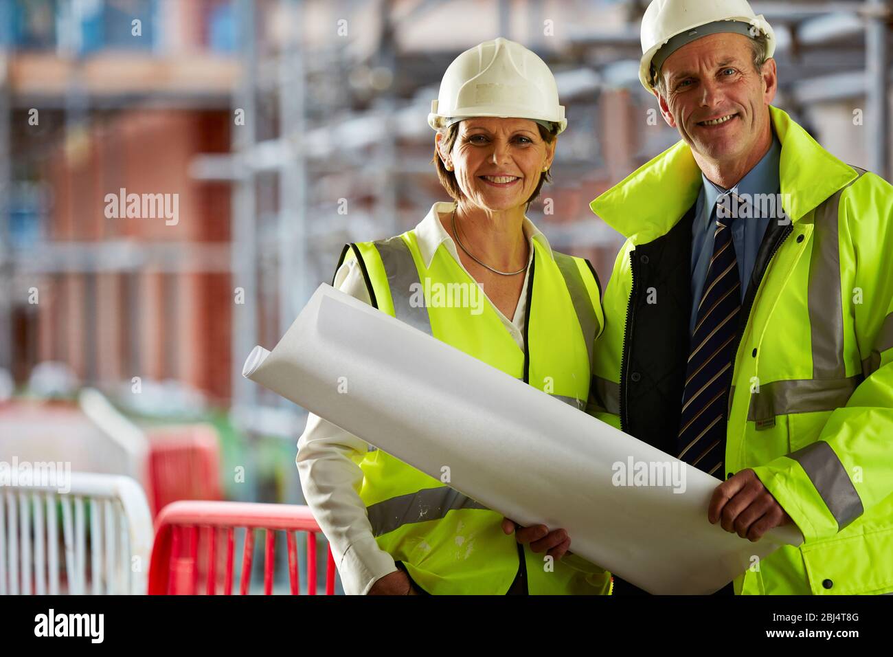 Porträt von zwei reifen Architekten in Schutzkleidung auf der Baustelle Blick auf Kamera hält eine Blaupause Stockfoto