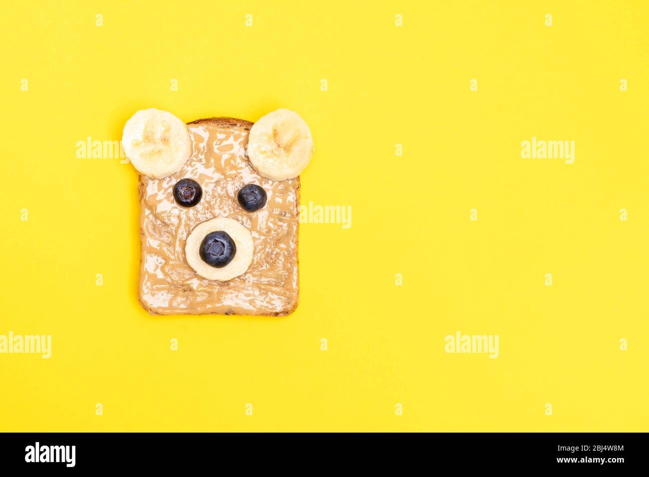 Lustige Kinder Frühstück Toast mit Erdnussbutter in Form von Bär mit Heidelbeere und Banane auf gelbem Hintergrund. Draufsicht, Kopierbereich Stockfoto