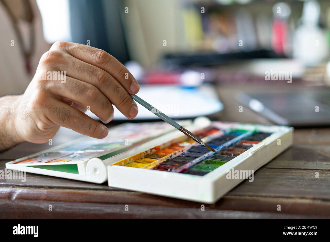 Mann Künstler Malerei mit Pinsel und Aquarell Palette auf Skizzenbuch. Nahaufnahme. Selektiver Fokus. Stockfoto