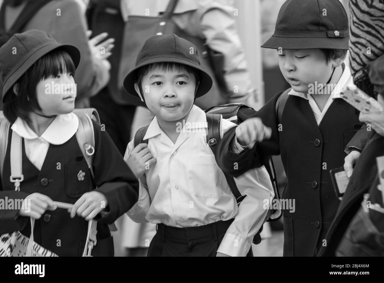 Drei japanische Kinder mit Schuluniformen laufen auf der belebten Straße neben dem Ameyoko-Markt in Tokio, Japan Stockfoto