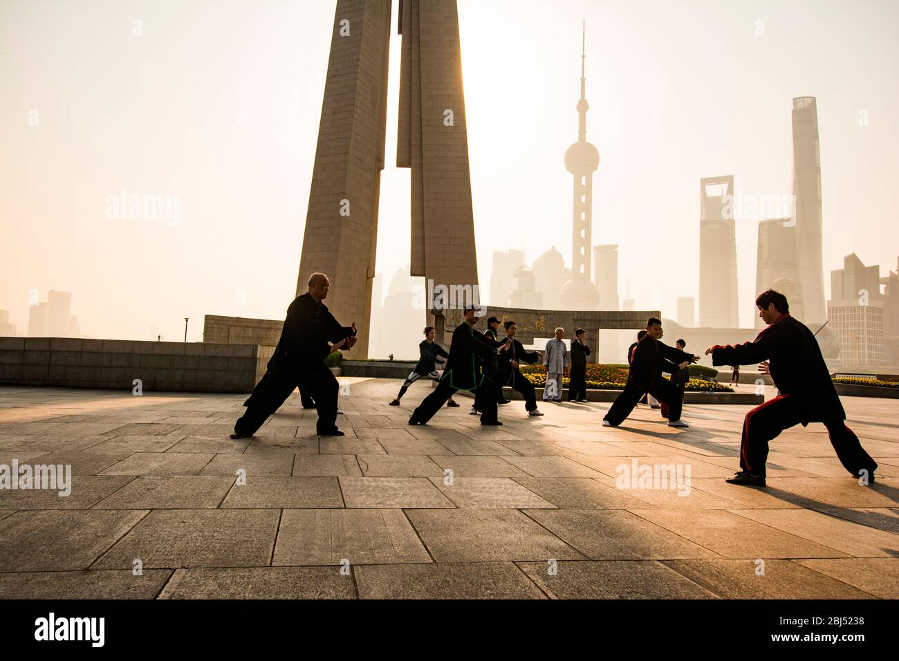 In Schwarz gekleidete Chinesen tun morgendliches Tai Chi vor dem Hintergrund moderner Wolkenkratzer. Stockfoto