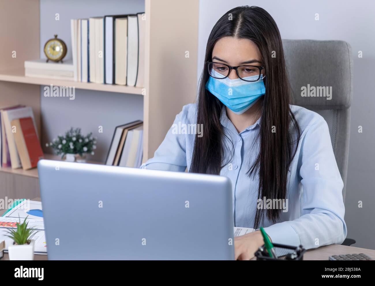 Geschäftsfrau mit Maske im Gesicht, die während der Coronavirus-Pandemie im Büro arbeitet. Arbeiten zu Hause während des Pandemiekonzepts. Stockfoto