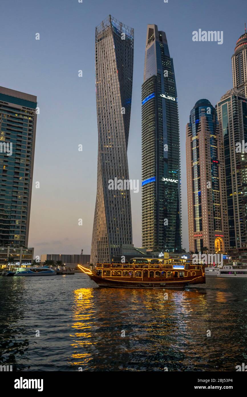 Eine leuchtende arabische Dhow führt bei einer luxuriösen Abendkreuzfahrt unter den imposanten Gebäuden der Dubai Marina vorbei. Stockfoto