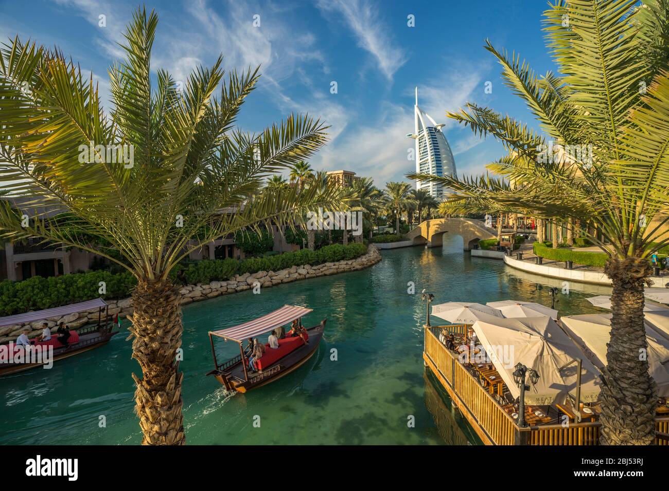 Arabische Abras gleiten durch das klare blaue Wasser des Souk Madinat Jumeirah, während das Segel wie Burj al Arab über dem Wasser aufsteigt. Stockfoto