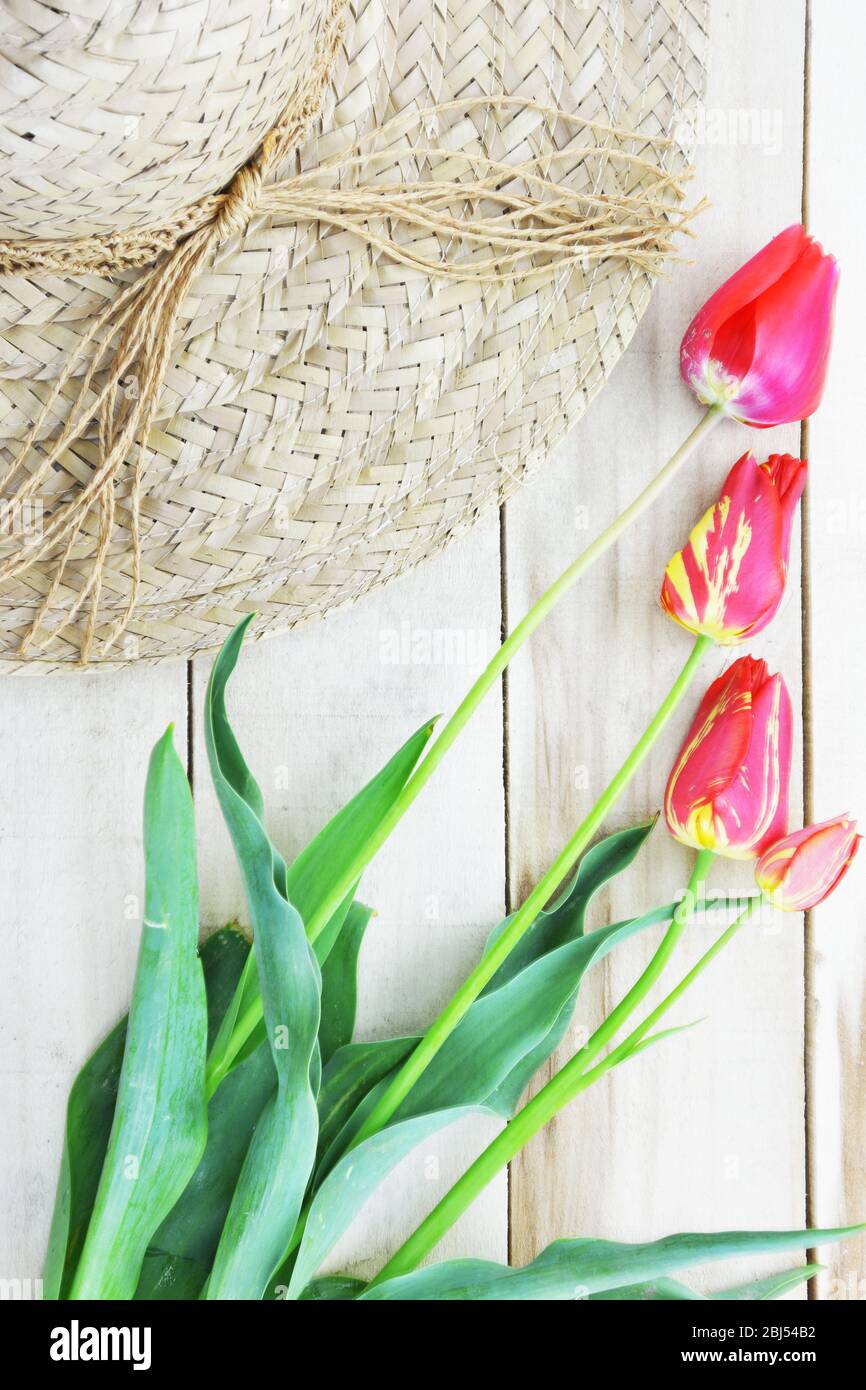 Rot und gelb gestreifte Tulpen und Strohhut auf Holztisch Stockfoto