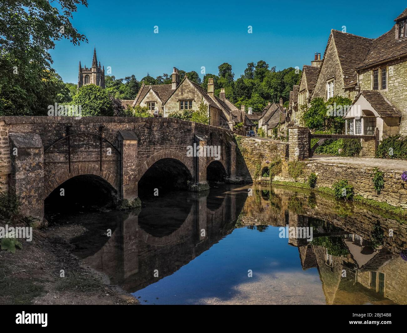 Eine Steinbrücke über einen sanften Bach führt den Weg in das Dorf Castle Combe in England. Stockfoto