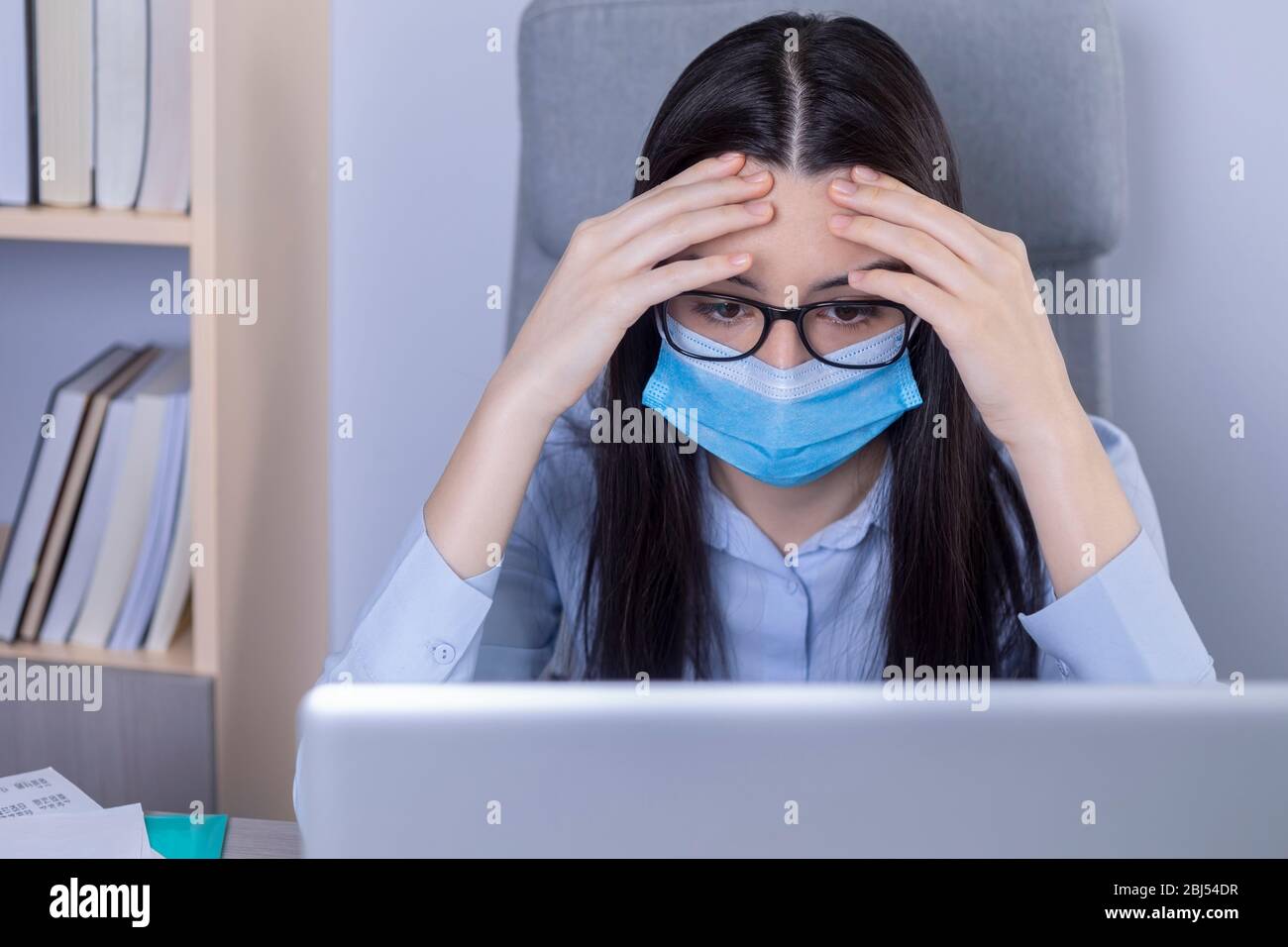 Erschöpfte Geschäftsfrau mit Maske im Gesicht, die während der Coronavirus-Pandemie im Büro arbeitet. Arbeiten zu Hause während des Pandemiekonzepts. Stockfoto