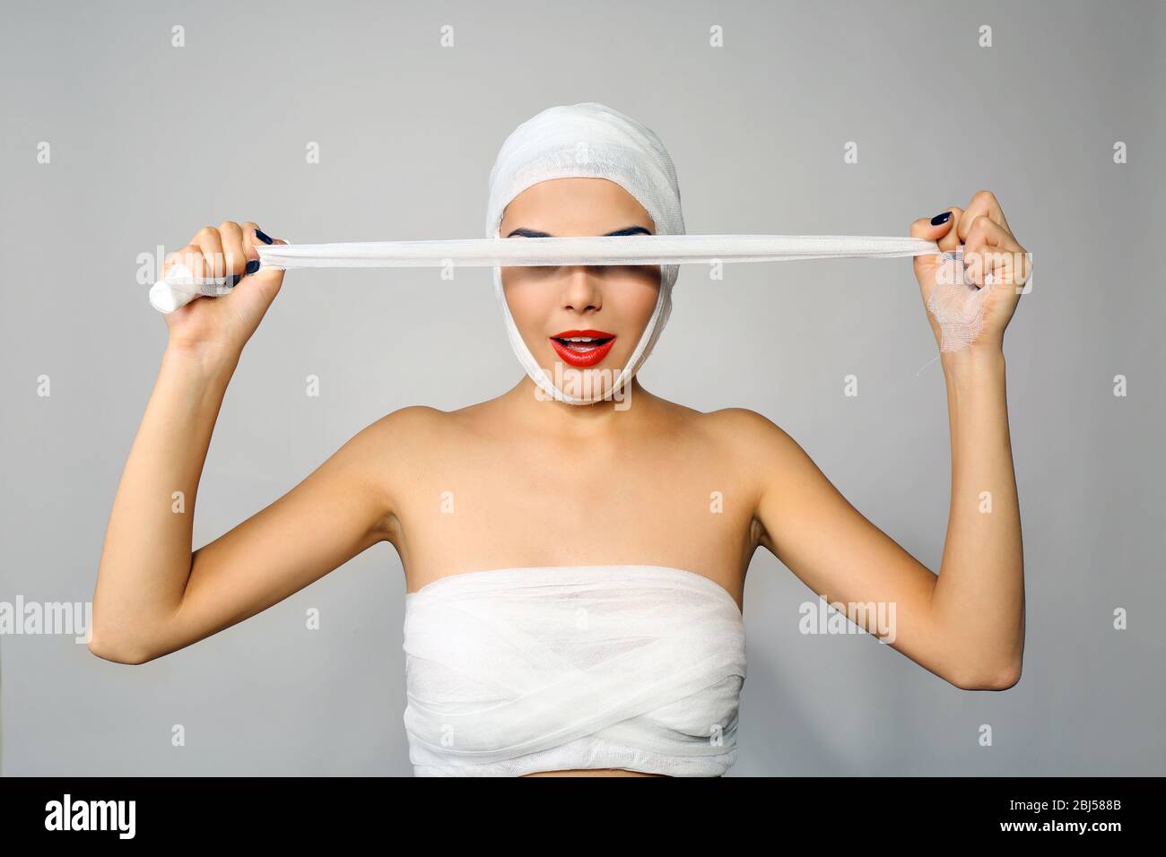Junge schöne Frau schließt ihr Gesicht mit Gaze, auf grauem Hintergrund Stockfoto